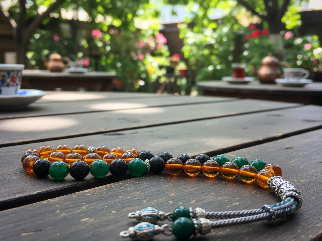 Close-up photo of a 33-bead tesbih made of natural stones on a wooden table in a sunlit Turkish garden setting