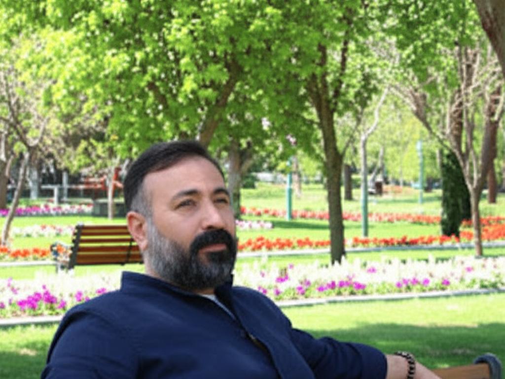 İstanbul parkında genç-orta yaşlı bir Türk adam, akik taşı bilekliği takmış ve çevresindeki doğa ile uyum içinde, huzurlu ve enerji dolu görünüyor.