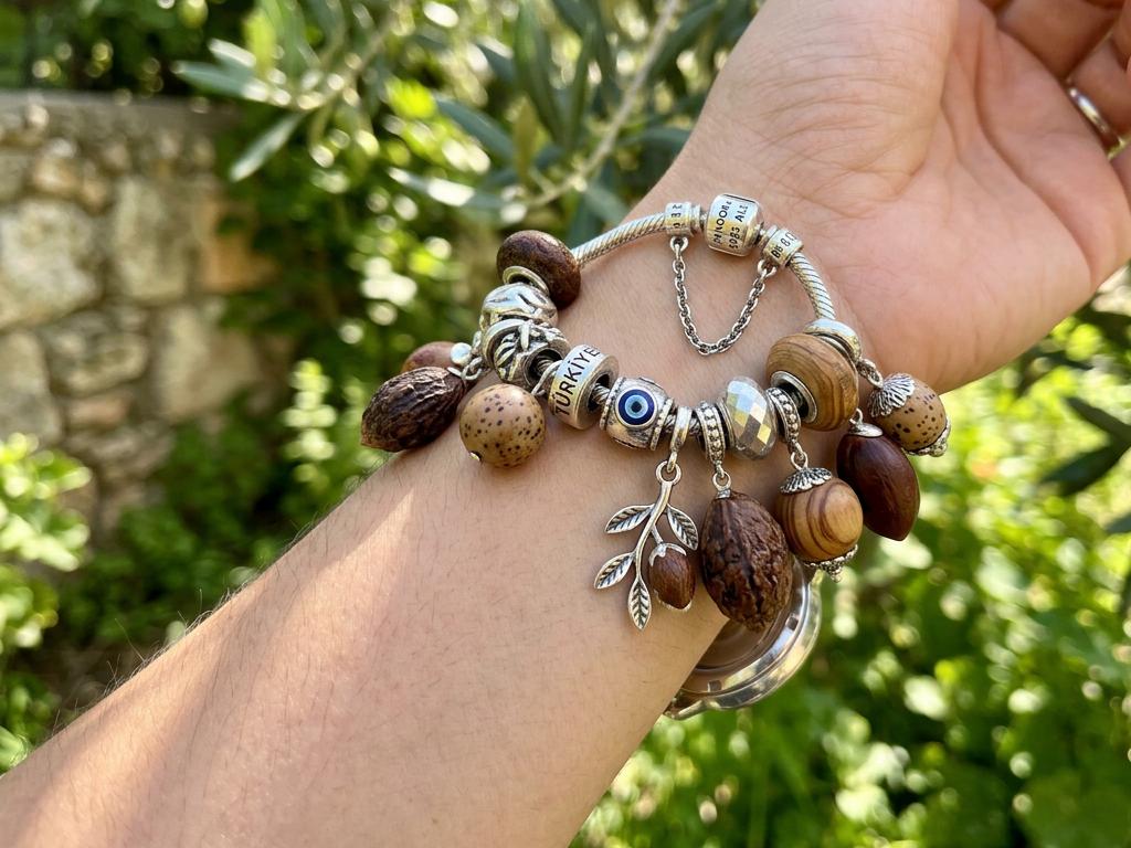 Doğal zeytin çekirdeği ve tesbih otu tohumlarından yapılmış charm’larla süslenmiş Pandora tarzı bilekliği taşıyan genç Türk kadınının bileği, doğal ışıkta bahçe arka planıyla foto-gerçekçi şekilde gösteriliyor.