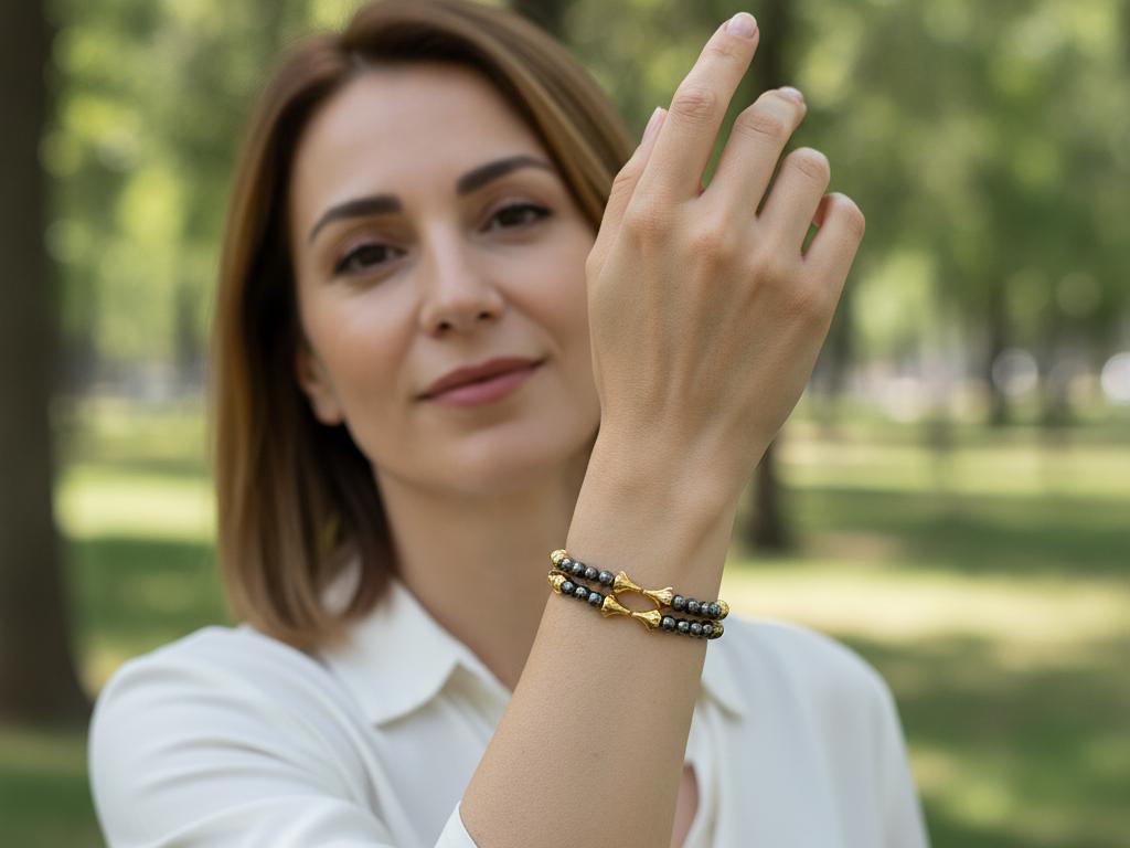 Park ortamında bir kadının bileğinde görünen çift iğde hatlı bileklik, doğal ışıkta öne çıkan sarı iğde ve koyu hematit taşlarıyla birlikte gösteriliyor. Sakin, şık ve gerçekçi bir yaşam tarzı takı çekimi.